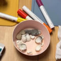 Kinder bemalen gesammelte Muscheln und Steine mit bunten Stiften.