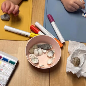 Kinder bemalen gesammelte Muscheln und Steine mit bunten Stiften.